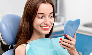 Young woman looking at her smile in mirror in dental chair