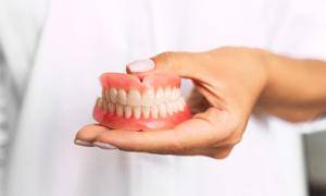 Person in white lab coat holding full dentures