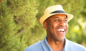 Man wearing blue shirt and fedora smiling and standing among trees