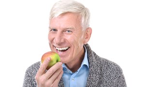 Happy man using implant denture to eat apple