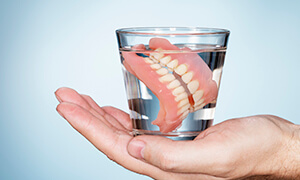 Hand holding dentures in glass of water